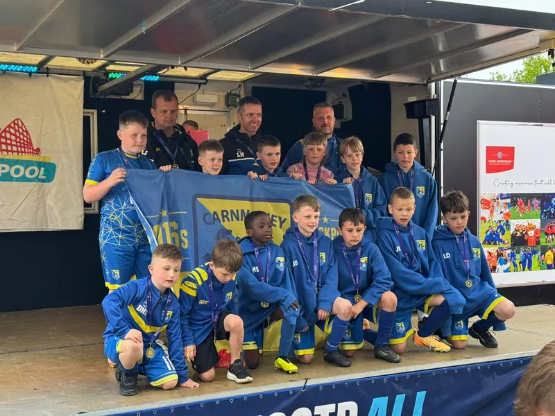 A squad and their coaches on the presentation stage with the flag and medals