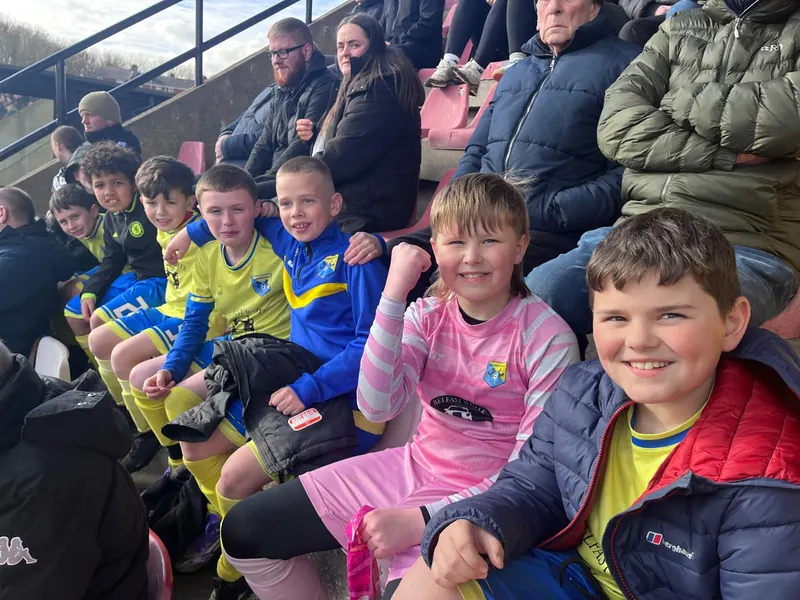 Children in kit in a stadium stand with their families