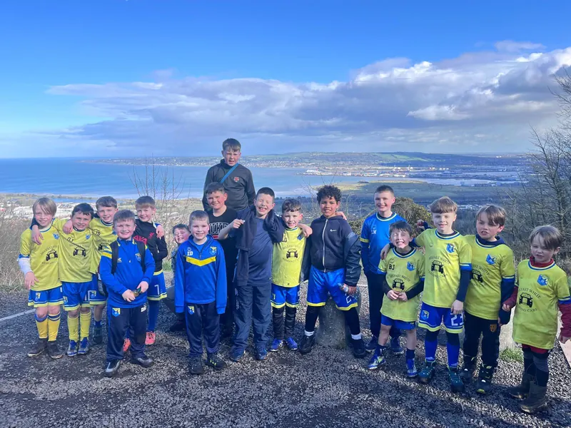 Children in kit and coats on Cave Hill in the sun, Belfast Lough behind