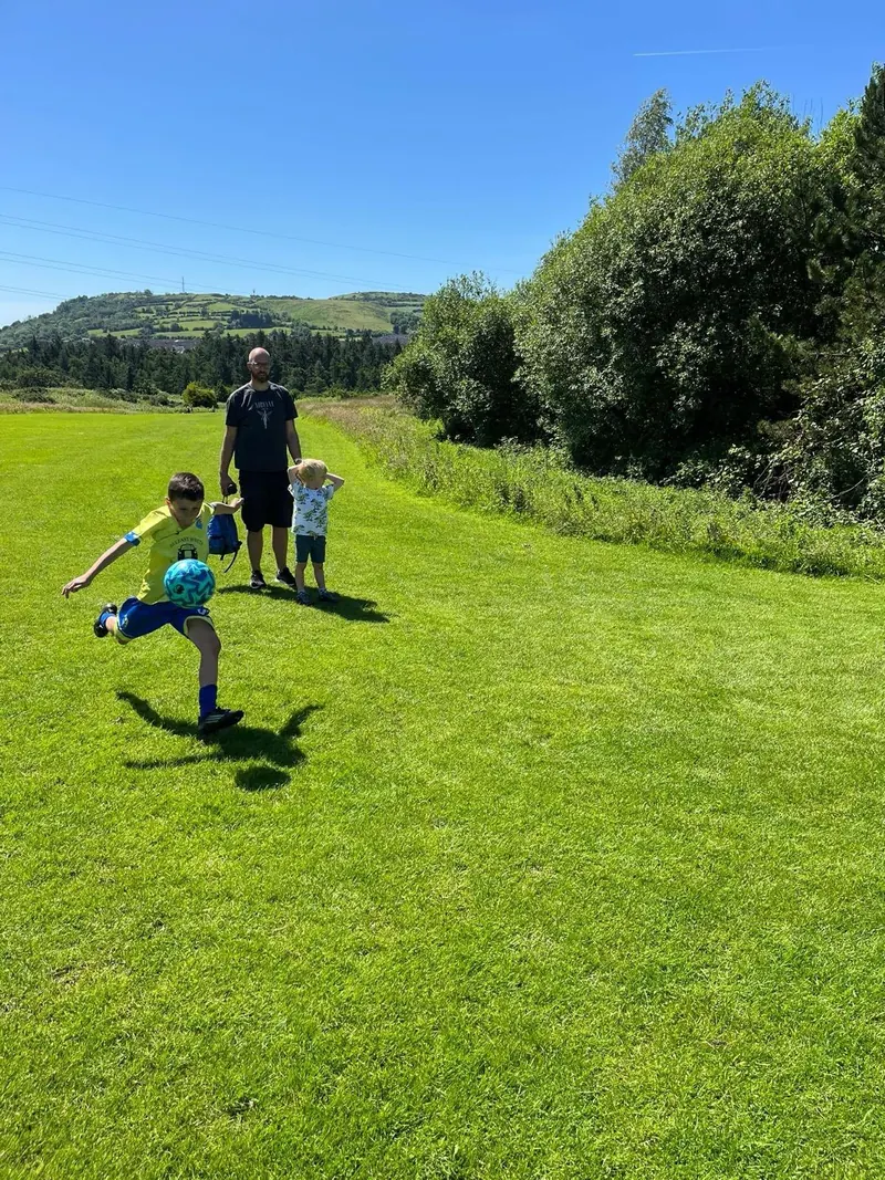 A child kicking a football across a sunny slope on the foot golf course