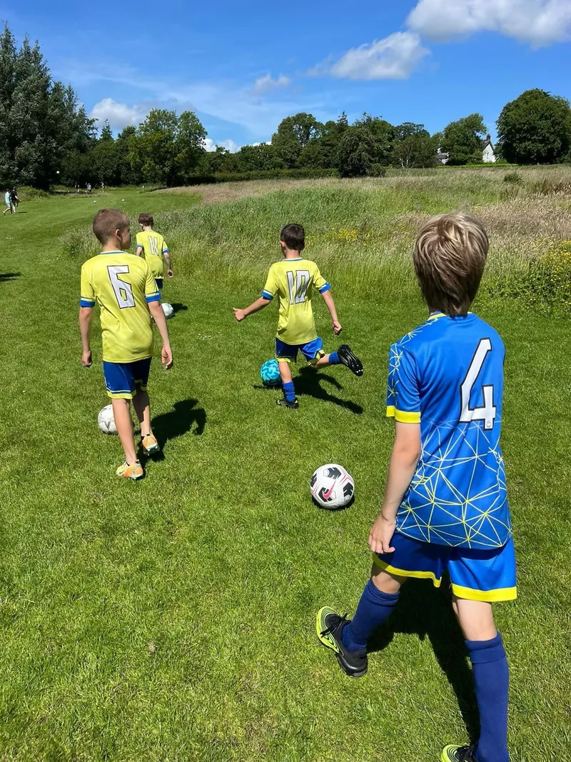 Children walking a foot golf fairway with their balls, seen from behind