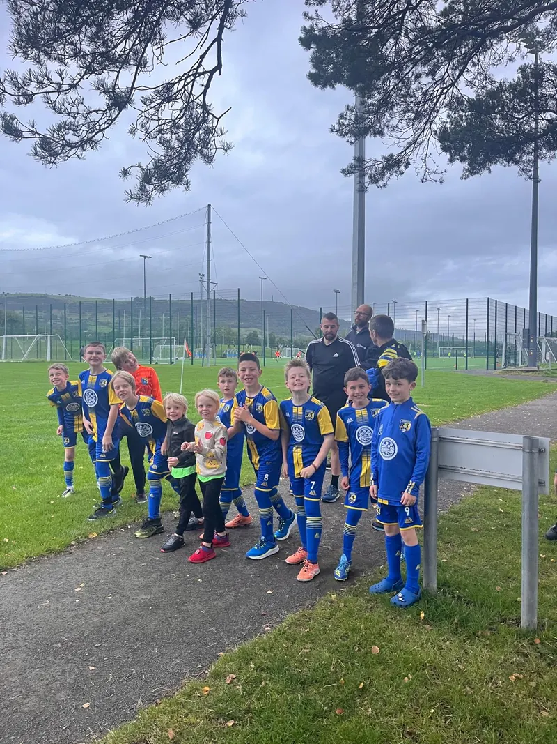 A squad in kit gathered on a path at the sports ground before a run, coaches behind them