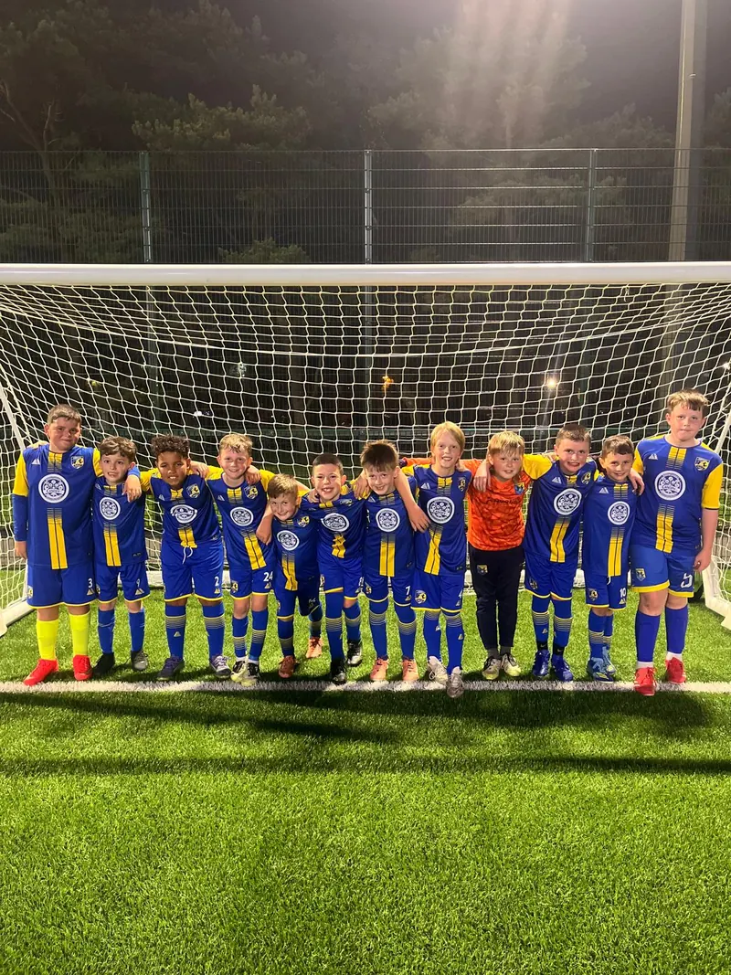 A squad in their brand new kit, arms round each other in a goal
