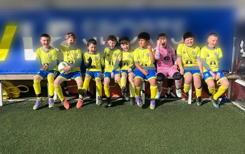 A squad in yellow kit sitting in a dugout, grinning and cheering