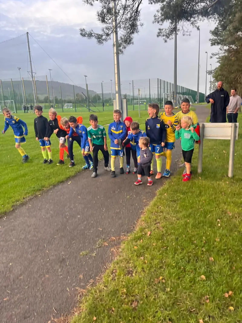 Children in different kits walking down a path at a sports ground, laughing